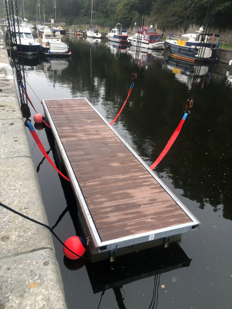Marina pontoon being lowered into the water via red strops