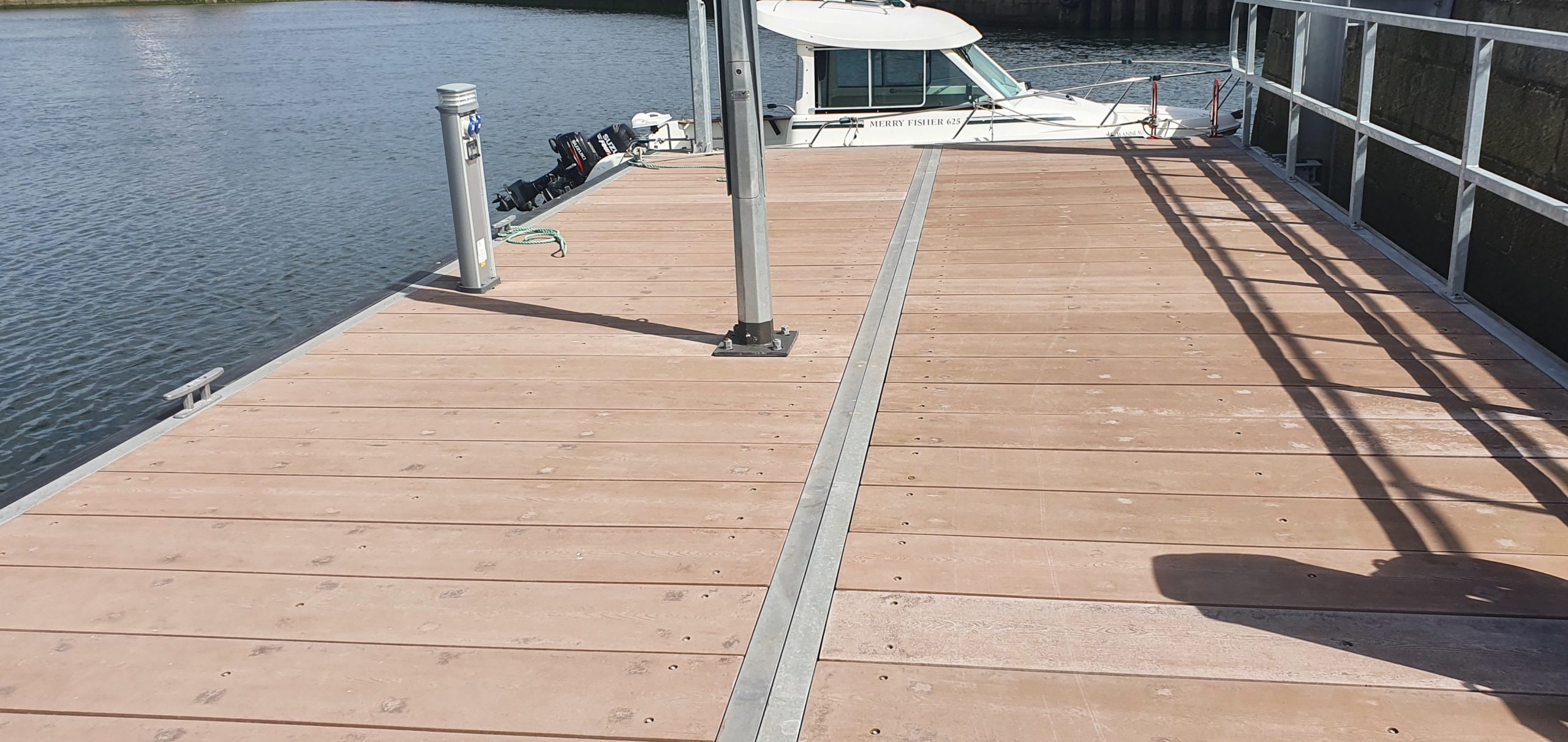 Marina pontoon with railing on right hand side and small power boat moored to the end