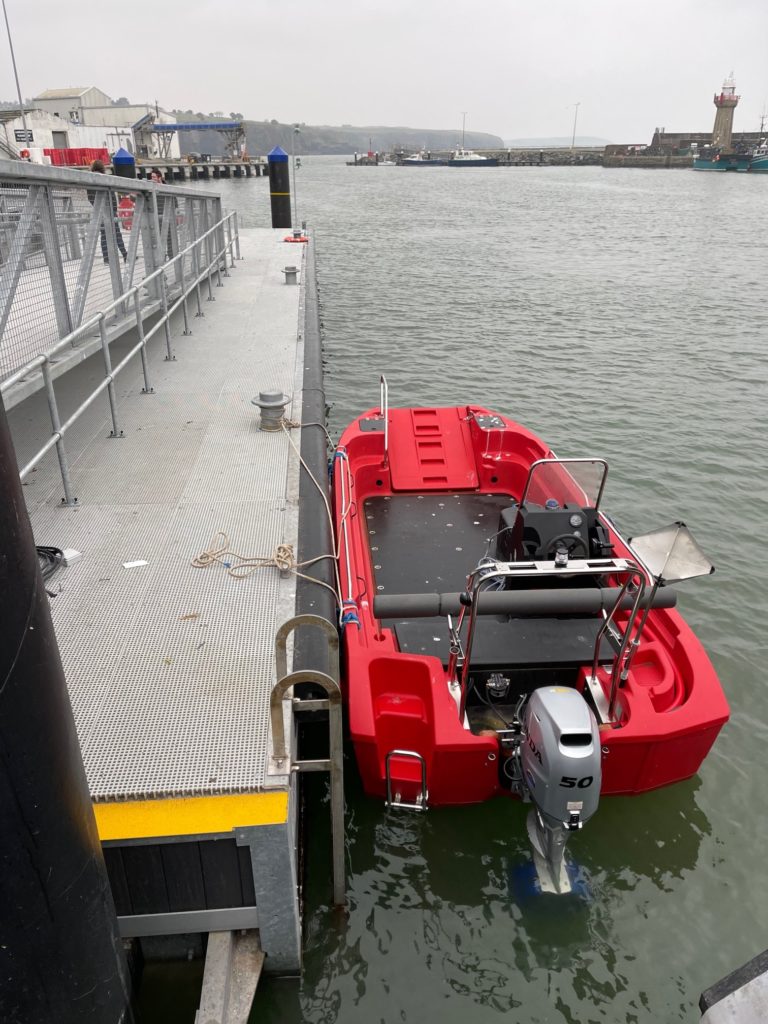 Small red motorboat with outboard engine tied alongside pontoon with safety ladder