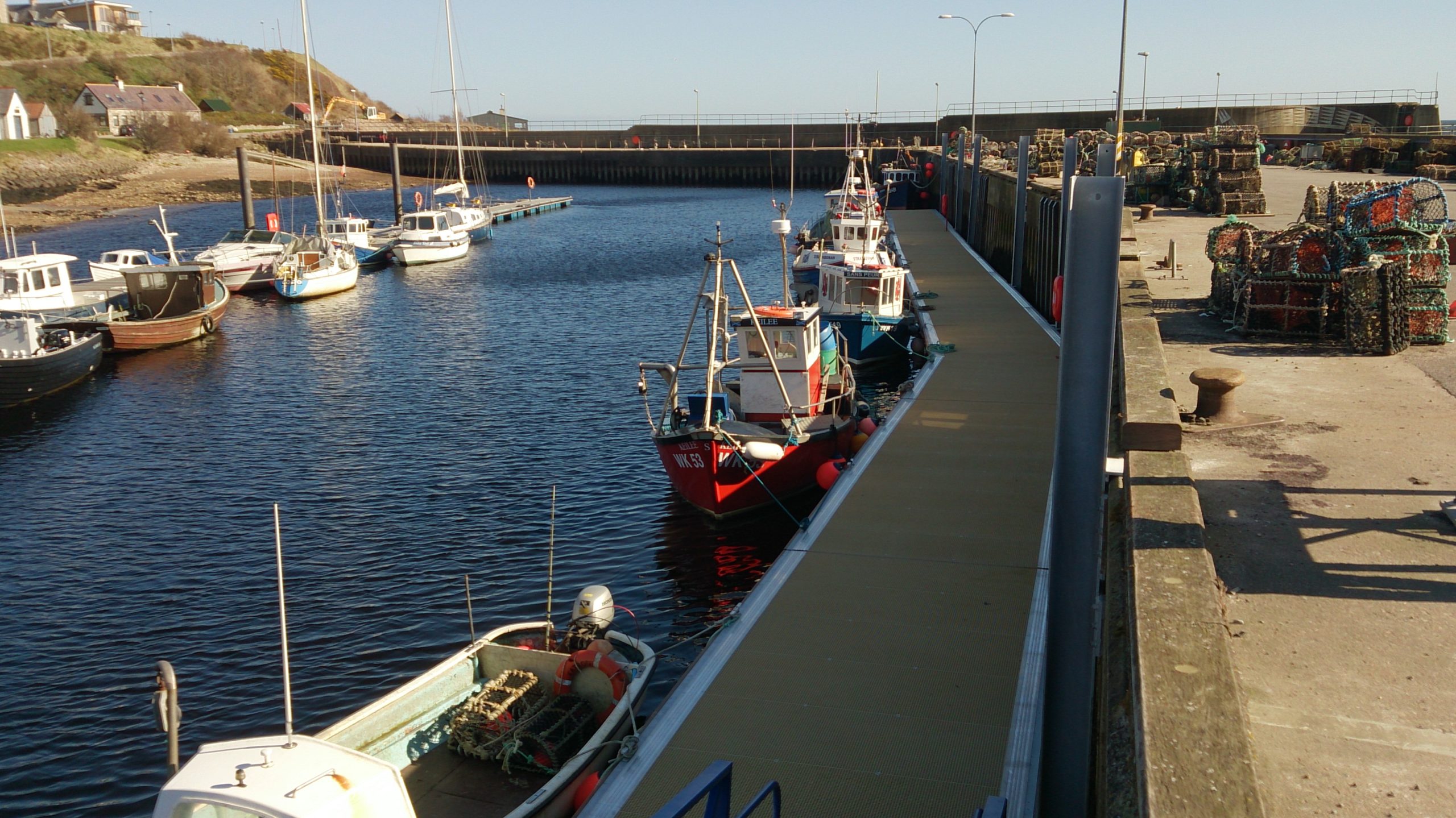 Pontoon curving alongside a quay wall with colourful fishing vessels moored