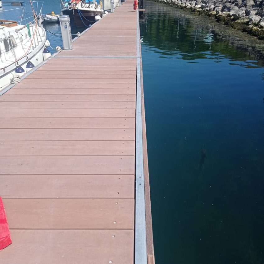 Terracotta coloured marina pontoon with sailing boat moored alongside