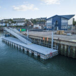 Grey GRC decked commercial pontoon with ramp alongside dock wall