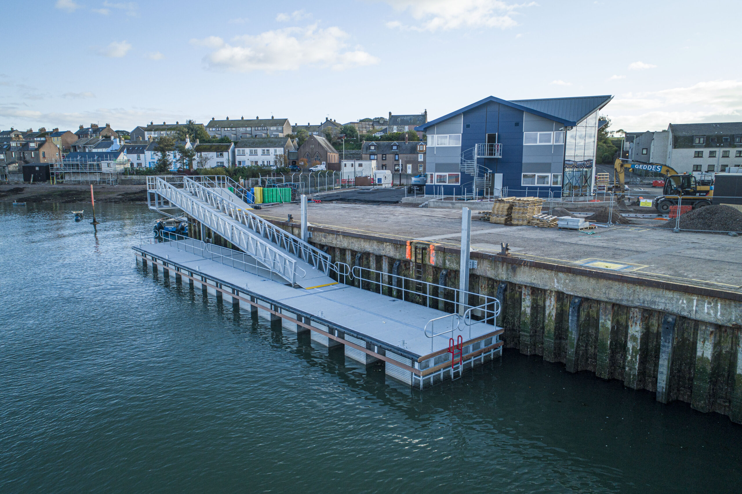 Grey GRC decked commercial pontoon with ramp alongside dock wall