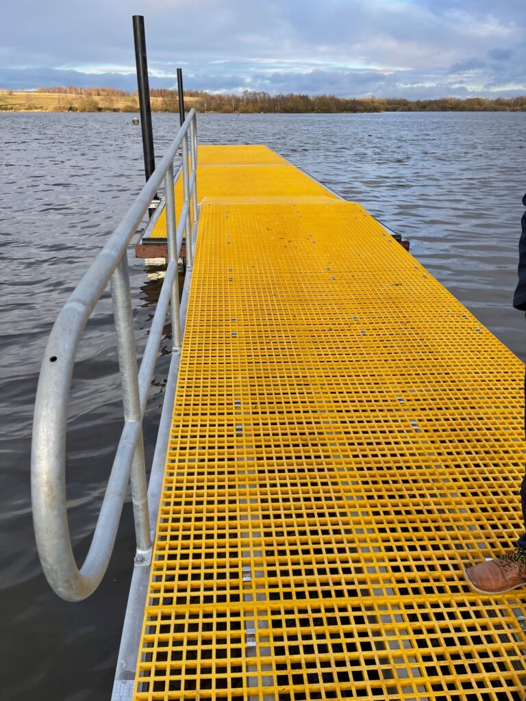 View along the length of yellow GRP decked watersports pontoon