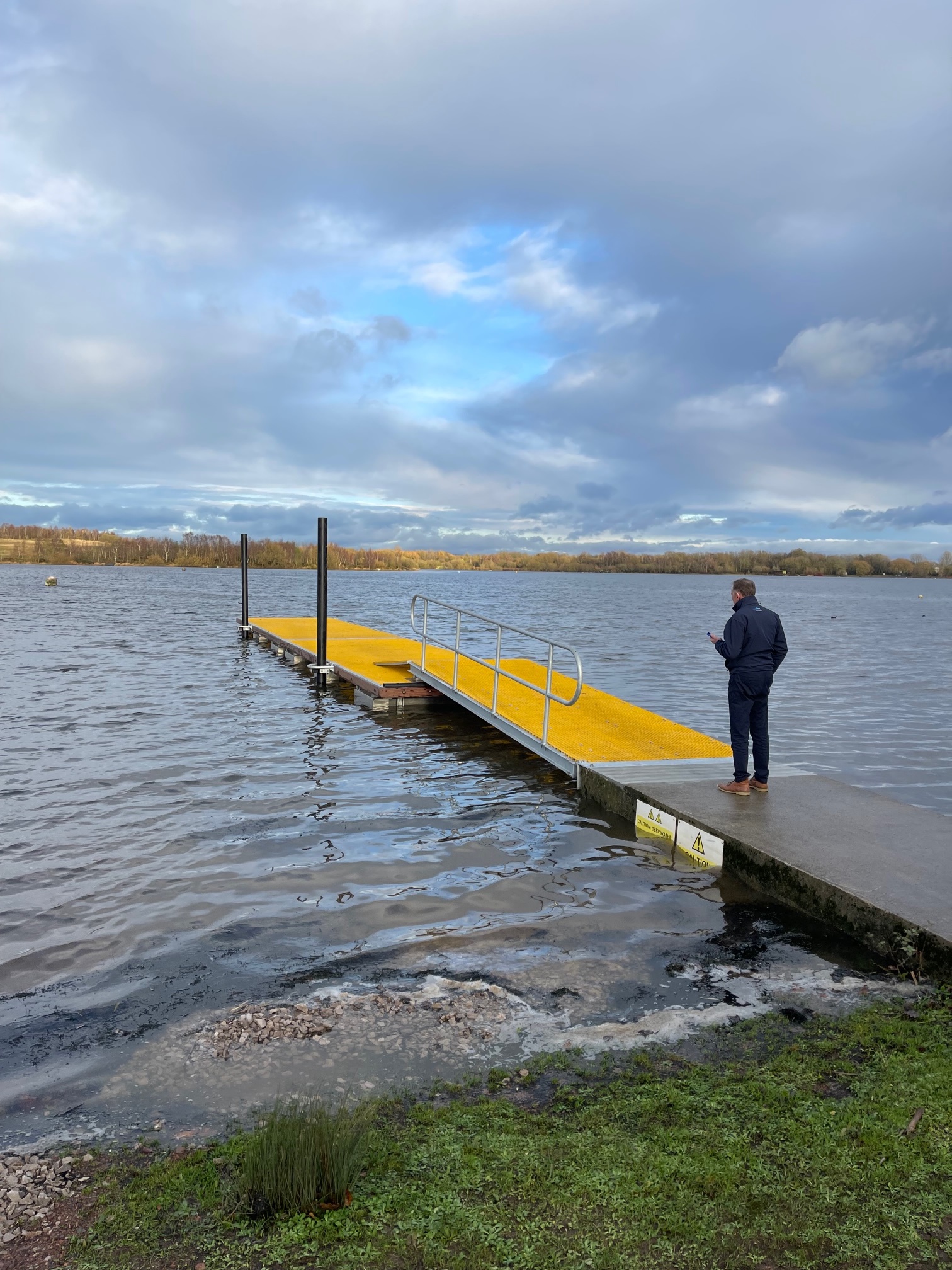 Person walking on yellow mini meshed GRP decked floating pontoon landscape view