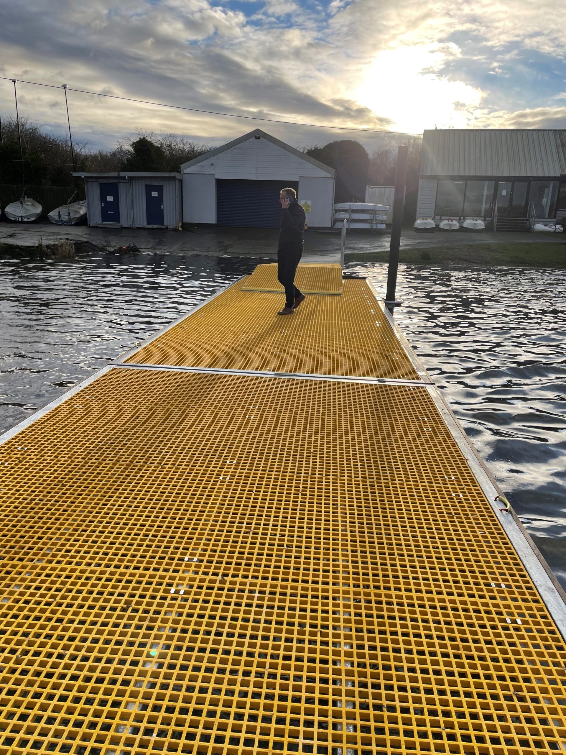 Person walking on yellow mini meshed GRP decked floating pontoon landscape view
