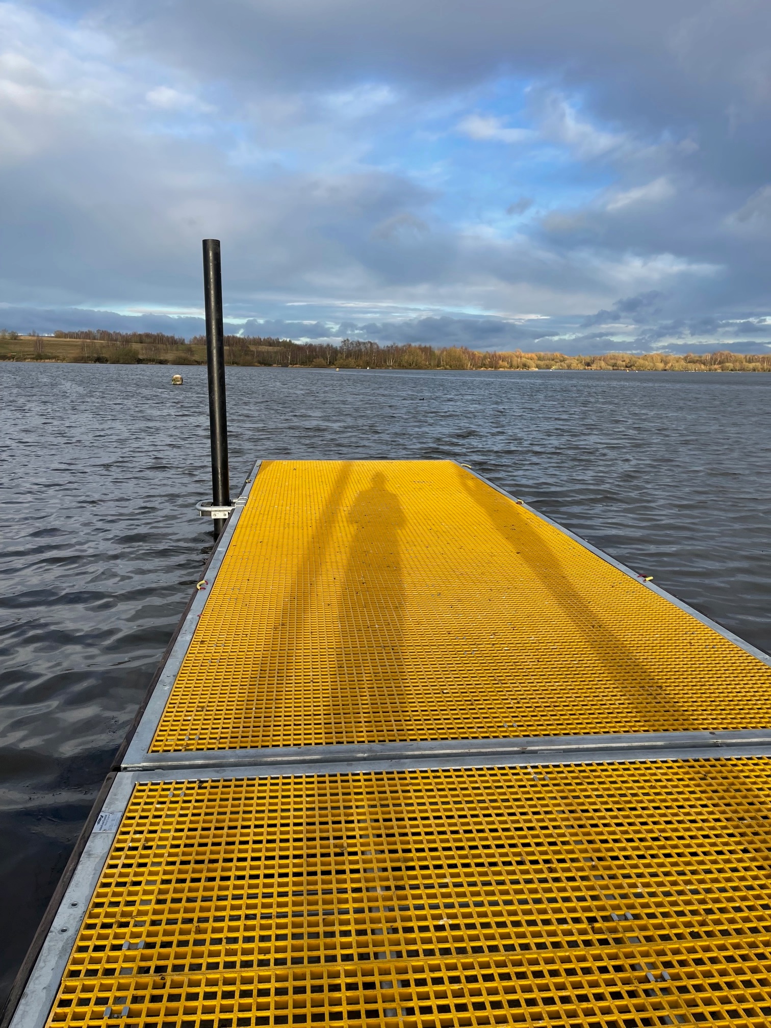 View along the length of yellow GRP decked watersports pontoon with pile