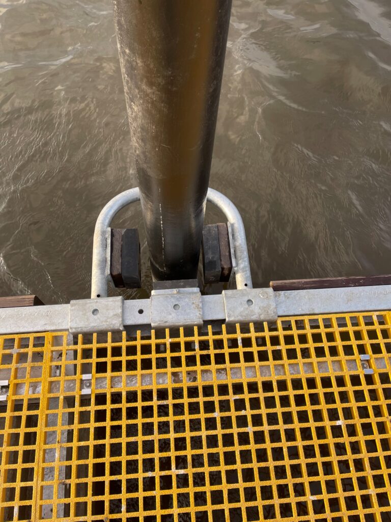 Pile mooring holding yellow GRP decked pontoon in place